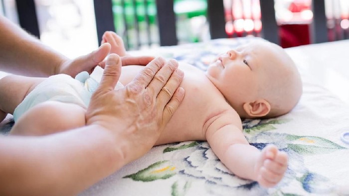 Doctor masseur massaging little baby, doing gymnastics at home. Baby massage.