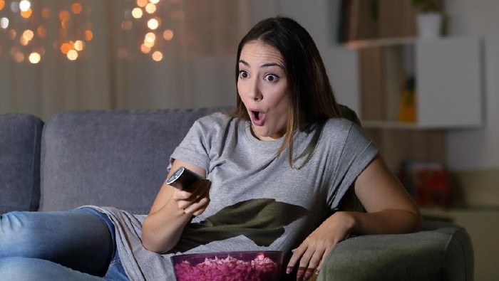 Amazed woman watching tv in the night sitting on a couch in the living room at home