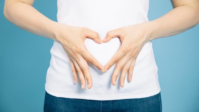 young woman who makes a heart shape by hands on her stomach.