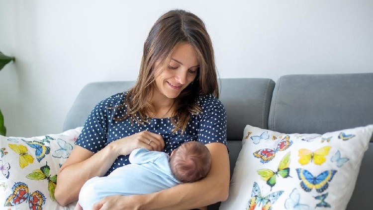 menyusui Young mother breastfeeding her newborn baby boy at home