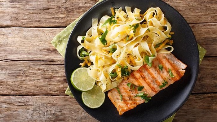Pasta fetuccini with cheddar cheese and grilled salmon on a plate close-up. horizontal view from above