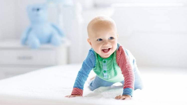 Baby boy crawling on bed. Little child playing in white sunny bedroom. Infant kid learning to crawl. Nursery for children. Textile, clothing and bedding for kids. Family morning at home.