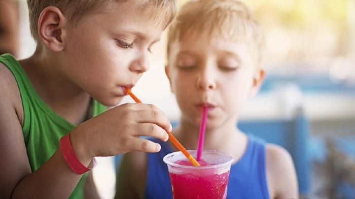 Closeup portrait of a little boys drinking a glass of colorful soda with crushed ice.