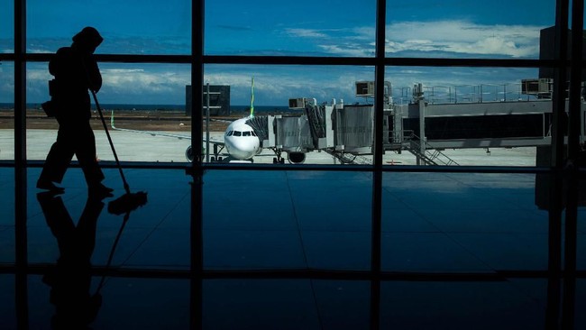 Siluet petugas kebersihan bekerja dengan latar belakang pesawat komersial maskapai Citilink terparkir di Yogyakarta International Airport (YIA) saat 