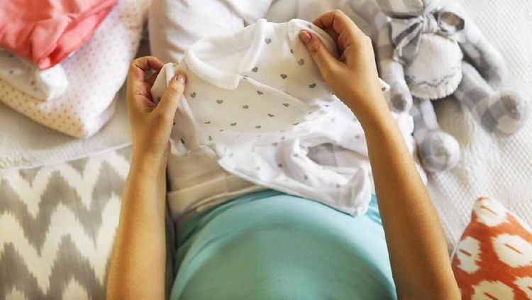Pregnant woman is packing baby clothes for going to maternity hospital top view