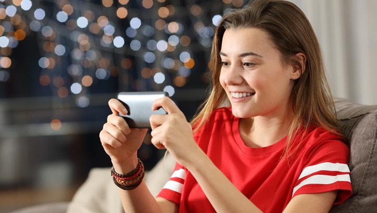 Teen watching media in a smart phone in the night sitting on a couch in the living room at home