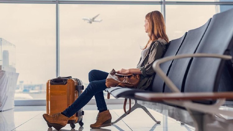 Start of her journey. Beautiful young woman looking out window at flying airplane while waiting boarding on aircraft in airport lounge