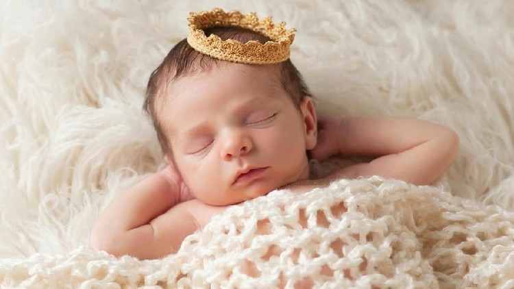 A newborn baby boy smiles as he wears a silver crown. A prince is born!