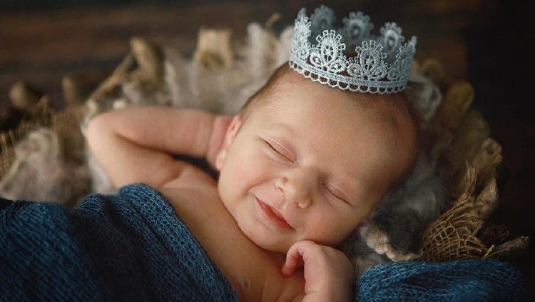 A newborn baby boy smiles as he wears a silver crown. A prince is born!