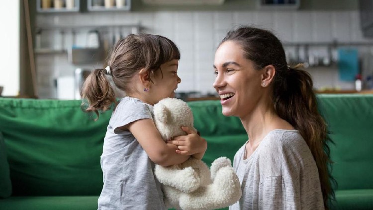 Smiling young loving mum talking with little preschool daughter with favorite stuffed toy, playing in living room at home, mother laughing with child, babysitter playing with pupil