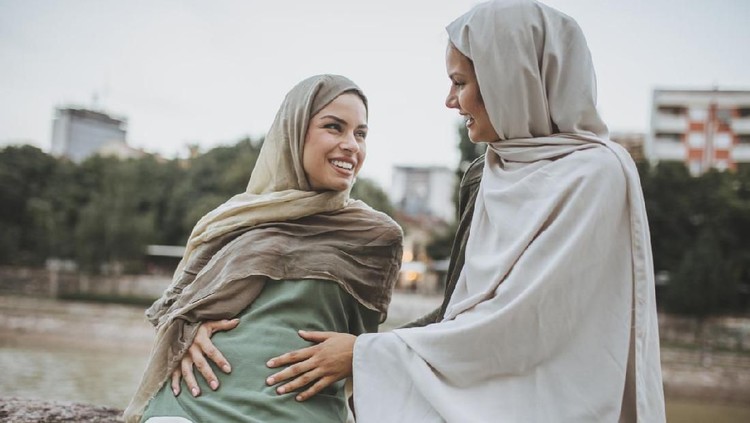 fidyah Smiling pregnant woman holding belly, resting on home sofa, maternity happiness