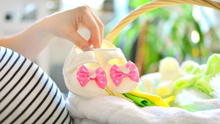 hamil Pregnant woman packing bag for maternity hospital at home. Preparing for girl newborn birth. Girl pink booties in female hand.