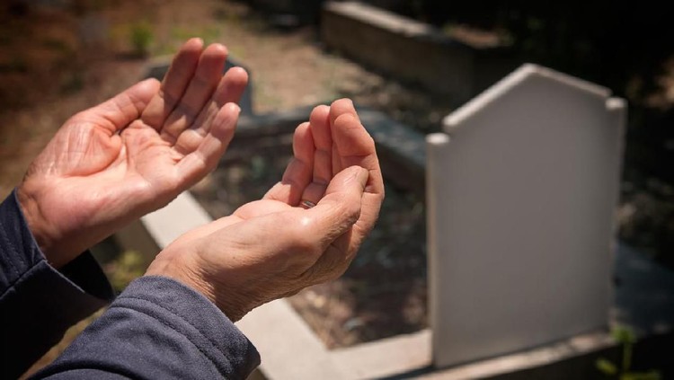 elderly muslim woman hands praying near the grave