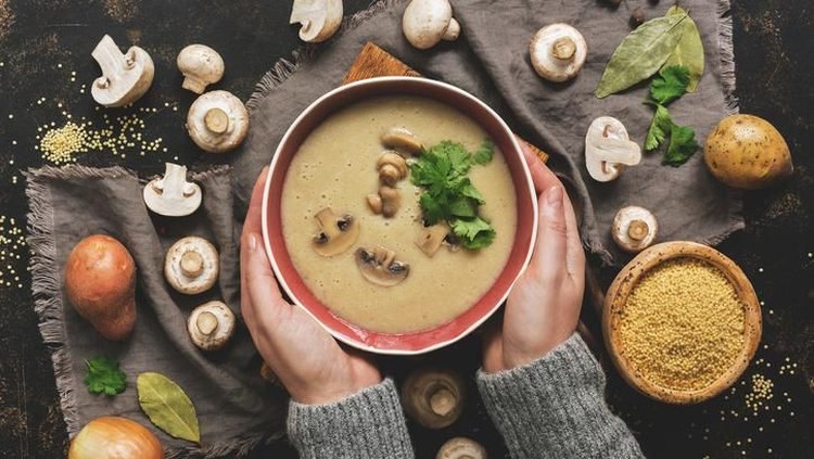 jamur Women hands in a gray sweater holding a bowl of cream of mushroom soup. Hot winter soup on a dark rustic background. Top view, flat lay