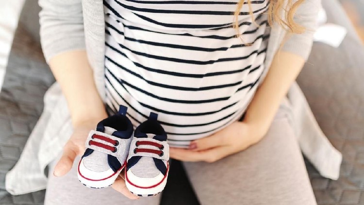 hamil Close up of pregnant Caucasian woman holding baby shoes and touching belly.