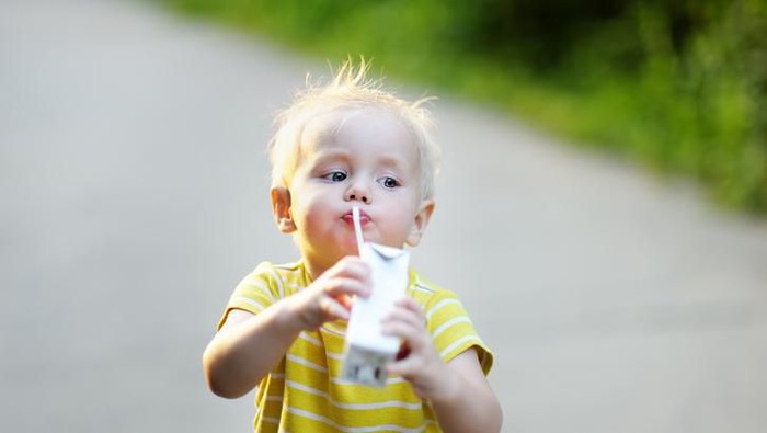 Color image of a little boy and a little girl sitting outside drinking a glass of milk and smiling at each other. Focus is on little boy.