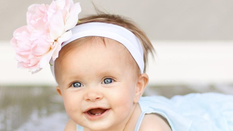 Baby girl in blue dress playing with bunch of pink tulips. Little child at home in sunny nursery. Toddler having fun with flowers