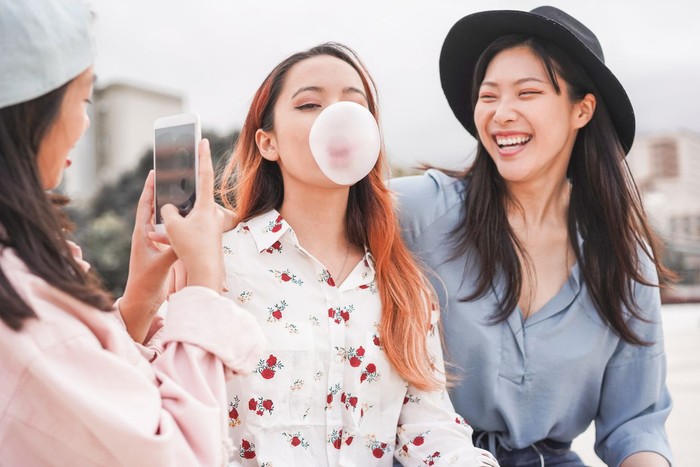 Trendy asian girls making video story for social network app outdoor - Young women friends having fun making live feed - New technology trends and friendship concept - Focus on person blowing
