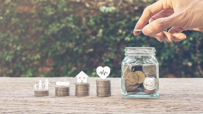 Savings money for family life concepts. Hand holding coin on a full money in glass jar and family member, car, house, healthy on coins. Depicts saving for wealth and life. fundraising concept.