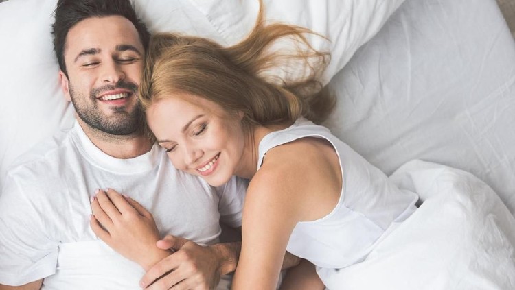 860618546 I am so happy with you. Top view portrait of cheerful young man and woman embracing while lying on bed. They are smiling with closed eyes
