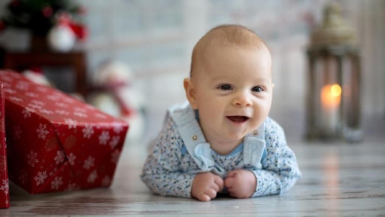Cute christmas portrait of little baby boy, lying on his belly on the floor, smiling happily, christmas decoration and presents around him