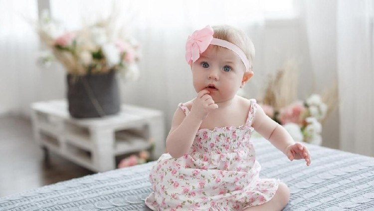 Charming beautiful lovely small female baby with plump cheeks creeps on bed, looks innocently on something, being naughty. Cute baby infant plays alone. Newborn kid crawls. Enthusiastic child