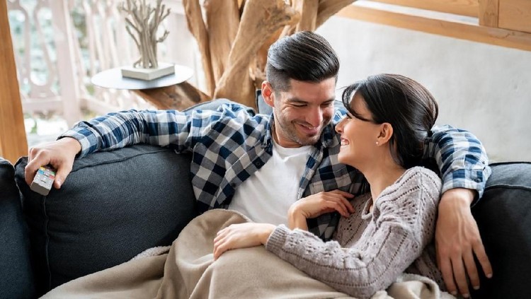 Portrait of a loving couple watching tv in their winter lodge while lying on the sofa looking very happy - lifestyle concepts
