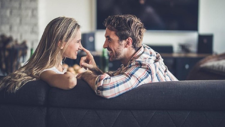 Young happy couple communicating on sofa in the living room while man is touching his girlfriend's nose.