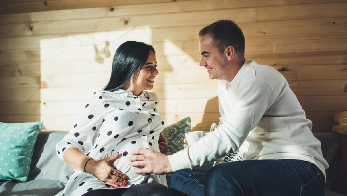 Man and woman, married couple relaxing together on sofa at home, woman is pregnant.