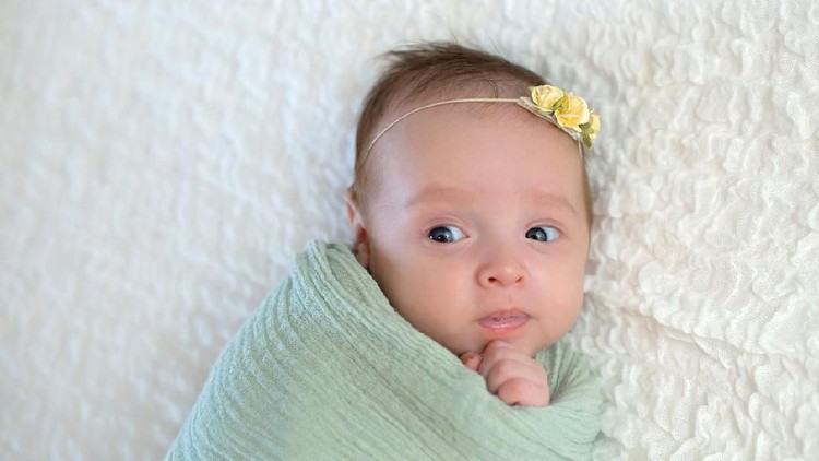 baby An alert 7 day old, Hispanic baby girl with a displeased look on her face. She is wrapped in a crocheted wool pouch and looking at the camera. Shot in the studio on a cream colored flokati (sheepskin) rug.