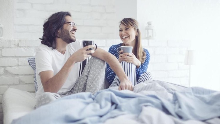 Beautiful happy young romantic girl brings breakfast to her husband in the bed and laughing together after he wakes up.