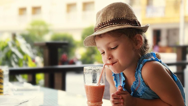 Cute little boy drinking orange juice with a help of his mother at home.