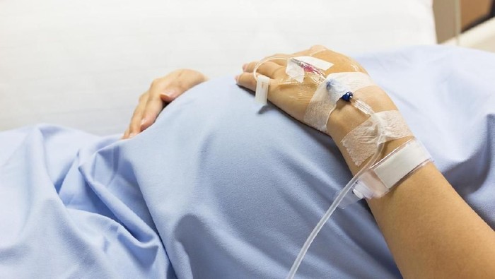 Asian Pregnant Woman patient is on drip receiving a saline solution on bed VIP room at hospital, selective focus.