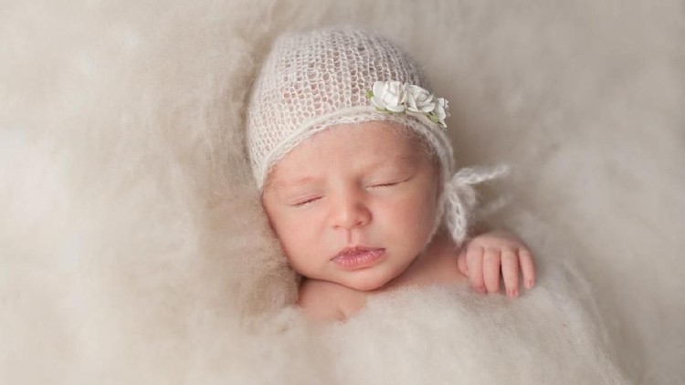 498945630 A portrait of a beautiful, two week old, newborn baby girl wearing a crocheted bonnet. She is smiling and sleeping on yellow colored fabric.