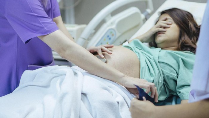 Doctor examining belly of expectant mother in hospital room. Thailand.