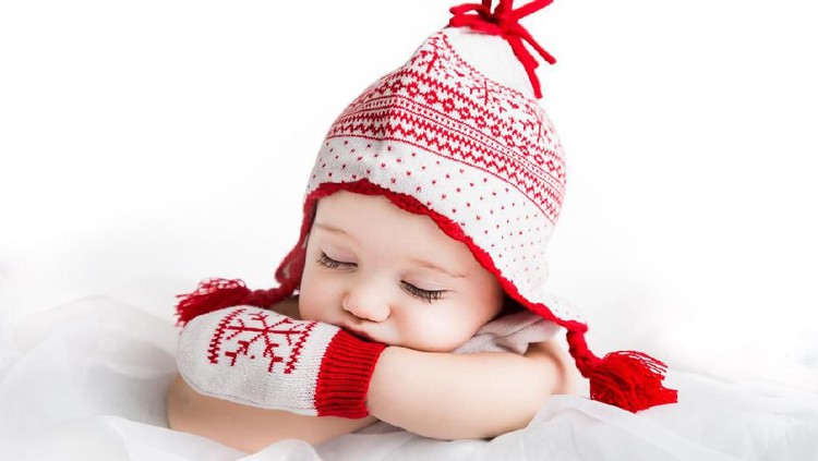 High key image of cute and beautiful sleeping baby wearing knitted festive red and white gloves with snowflake motiv and matching hat. Christmas, winter and New Year theme. Shot with Canon EOS 6D, Tamron  24-70 mm f2.8, indoor studio lighting.