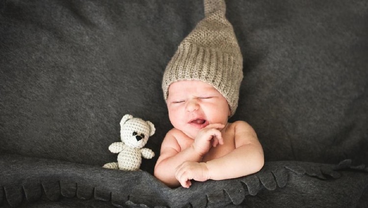 A newborn baby smiles as he hugs a toy bunny. He is seven days old.