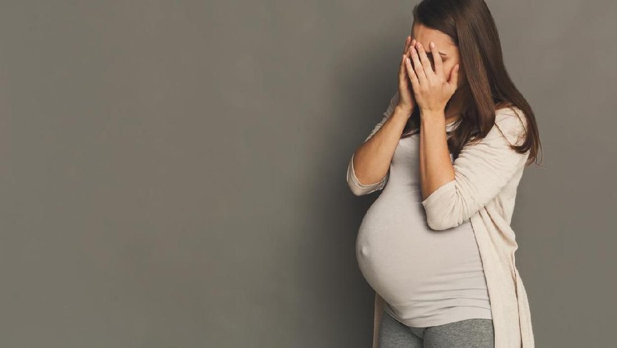 Pregnant woman holding her belly, looking through window