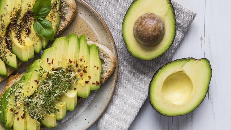 Toast with sliced avocado topping, basil leaf and seasoning.