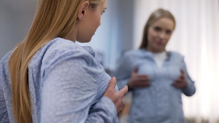 Portrait of female doctor choosing mammary prosthesis with her patient over white background.
