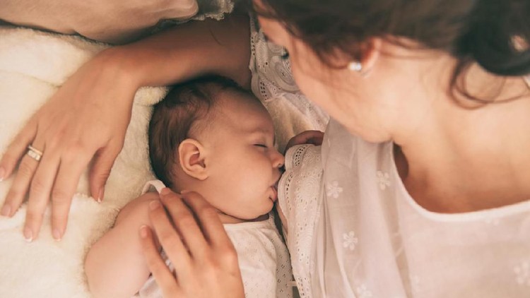 menyusui Beautiful young mom breastfeeding her 5 months baby. Mather nursing baby. Family at home.