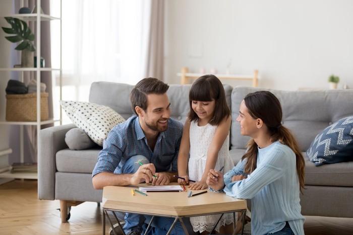 Happy family with kid playing together, caring mom and dad smiling teaching little daughter to draw with color pencils, mother and father having fun with cute child help in creative weekend activity