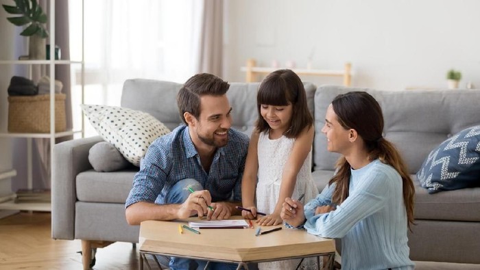 Happy family with kid playing together, caring mom and dad smiling teaching little daughter to draw with color pencils, mother and father having fun with cute child help in creative weekend activity