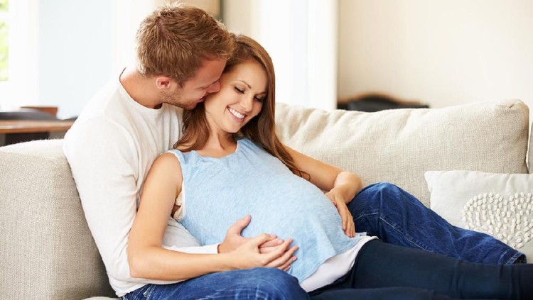 Couple With Pregnant Woman Relaxing On Sofa Together