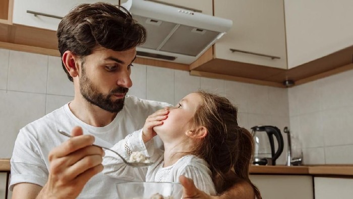Family relationship.. Food. Parenthood. Dad is feeding his little daughter who is refusing to eat. In the kitchen at home
