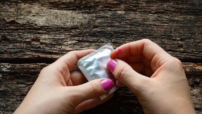 young woman pierces a condom