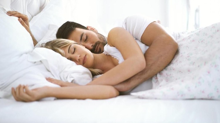 Chic mature husband and wife resting in bedroom lying down and embracing in bed