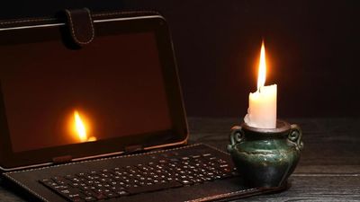 Blackout concept. Lighting candle near laptop with dark empty screen