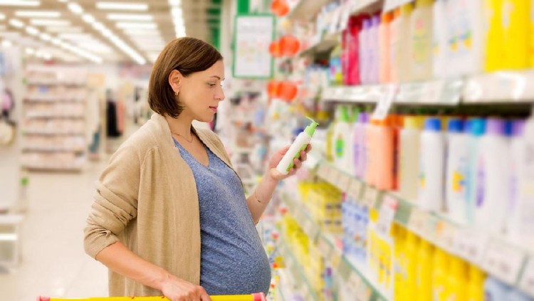 Young pregnant woman applying cream onto skin in bathroom