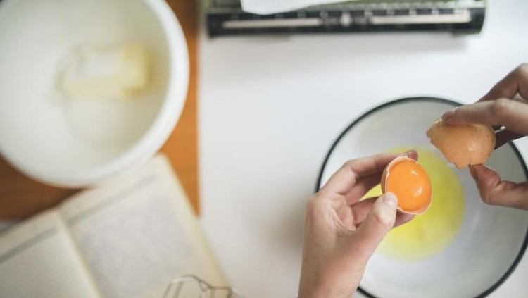 Female hands holding cracked egg over a white bowl